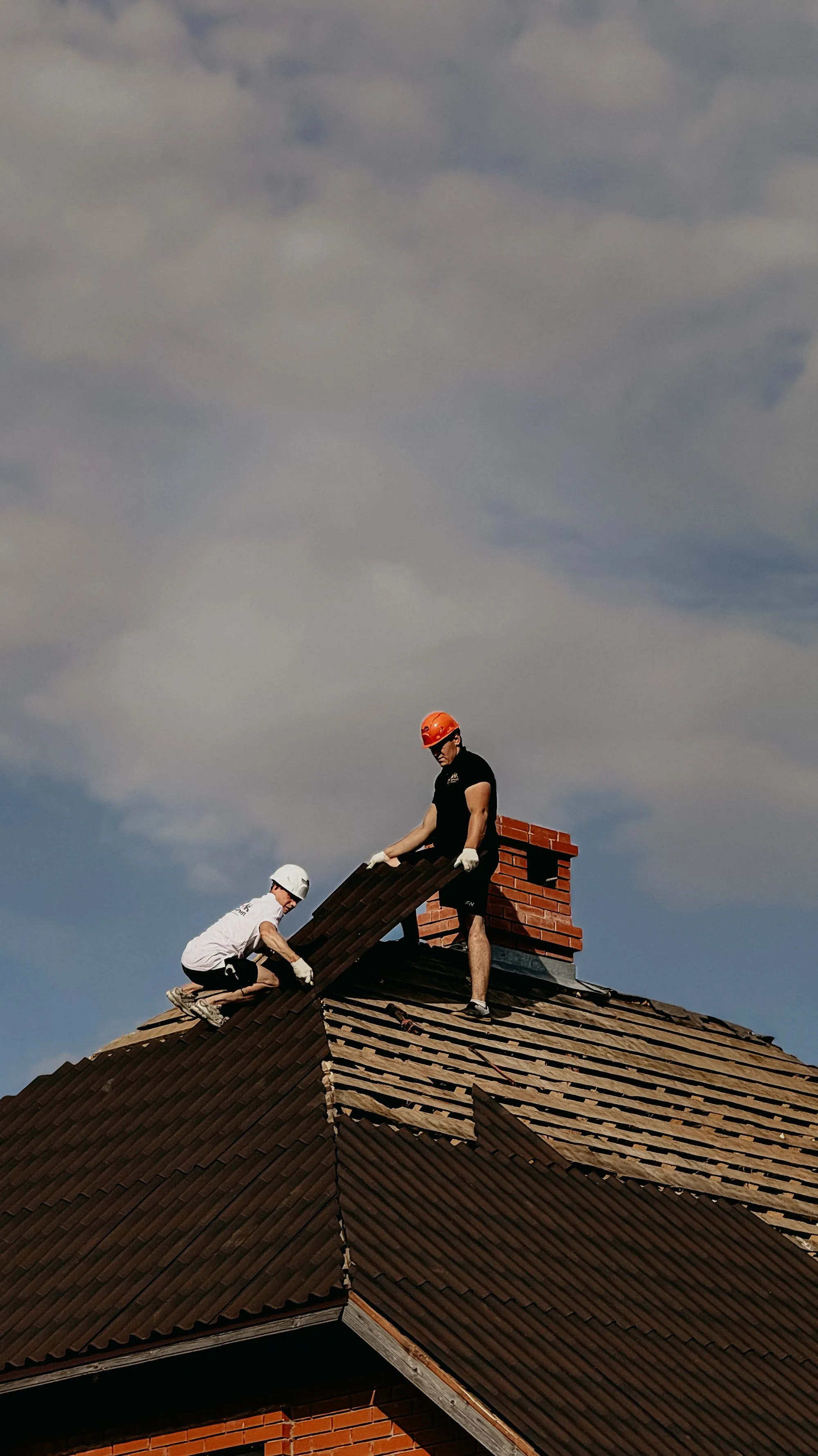 Two roofing crew members fitting new covering along a residential roof