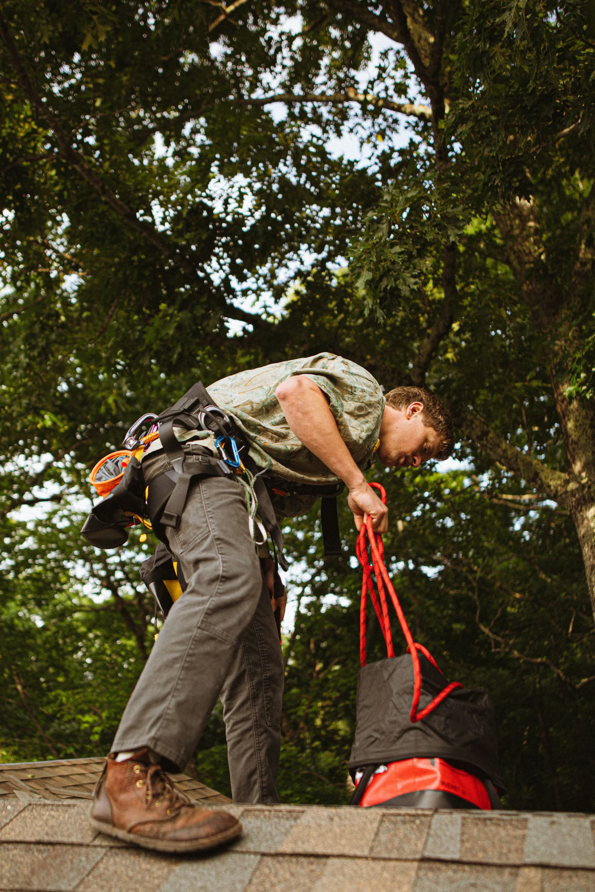 A roofer in a safety harness working across a shingled roof slope