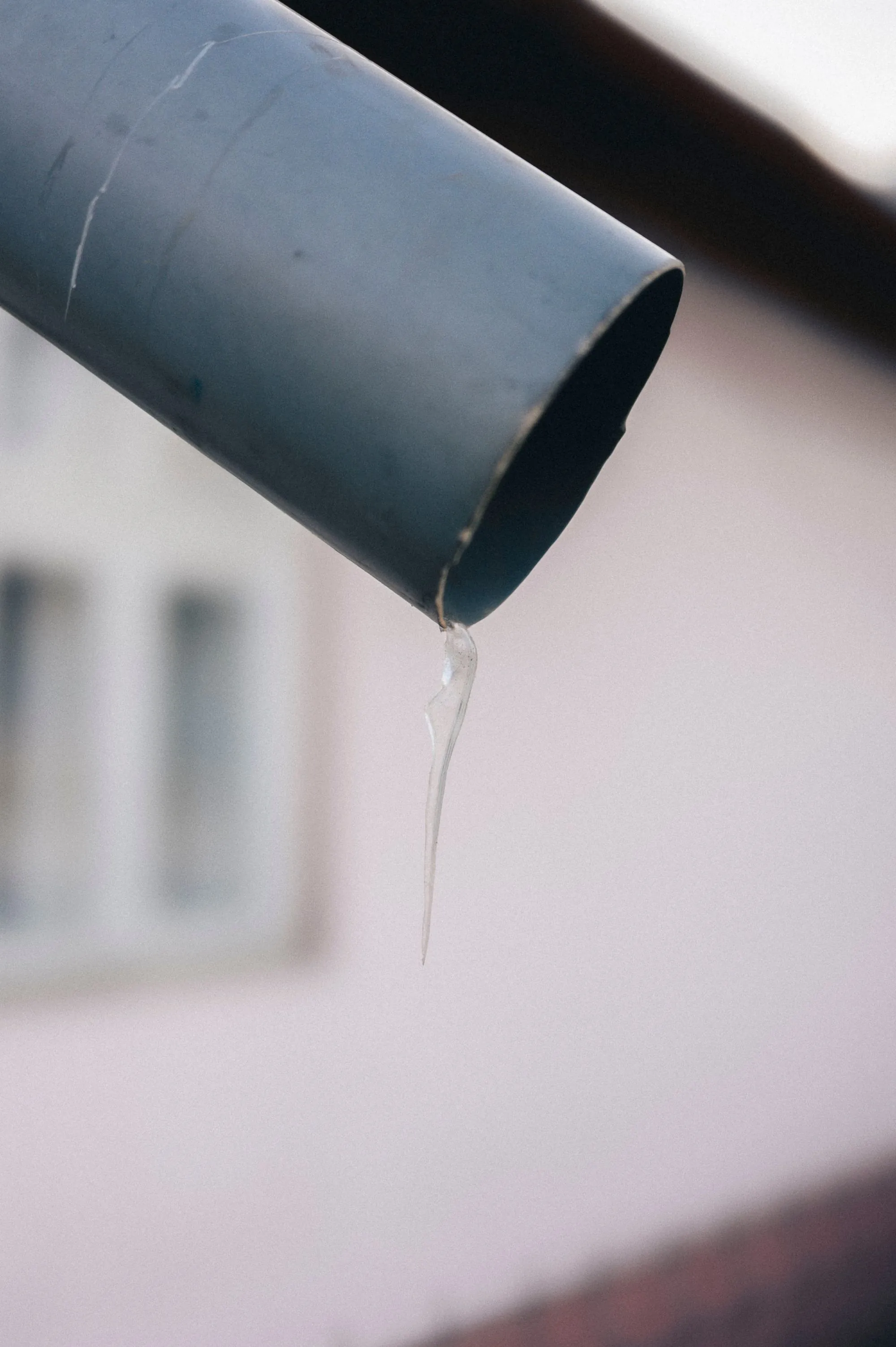 A metal downspout discharging rainwater beside a house wall