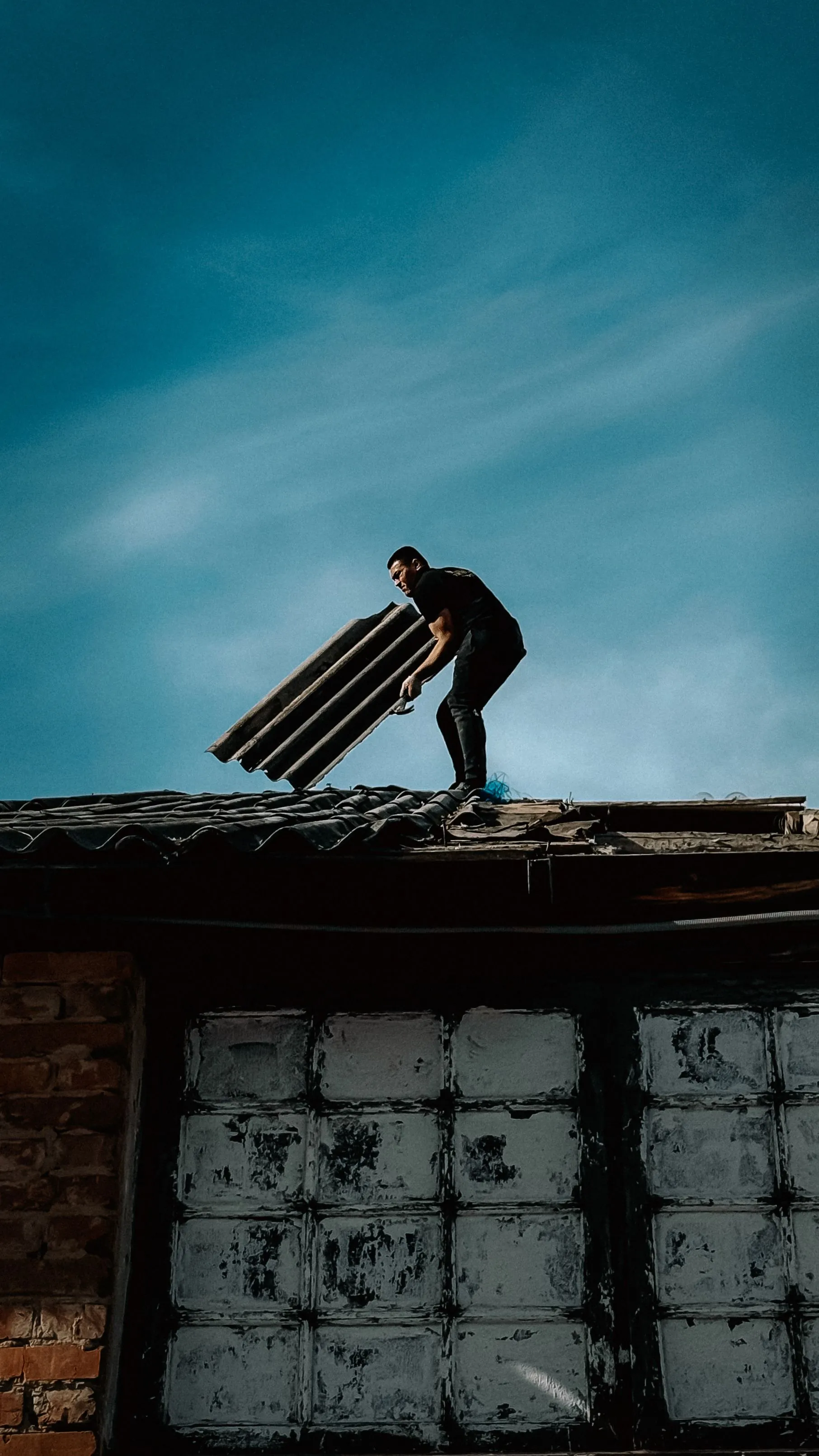A roofer lifting old roofing off a stripped roof deck during a replacement