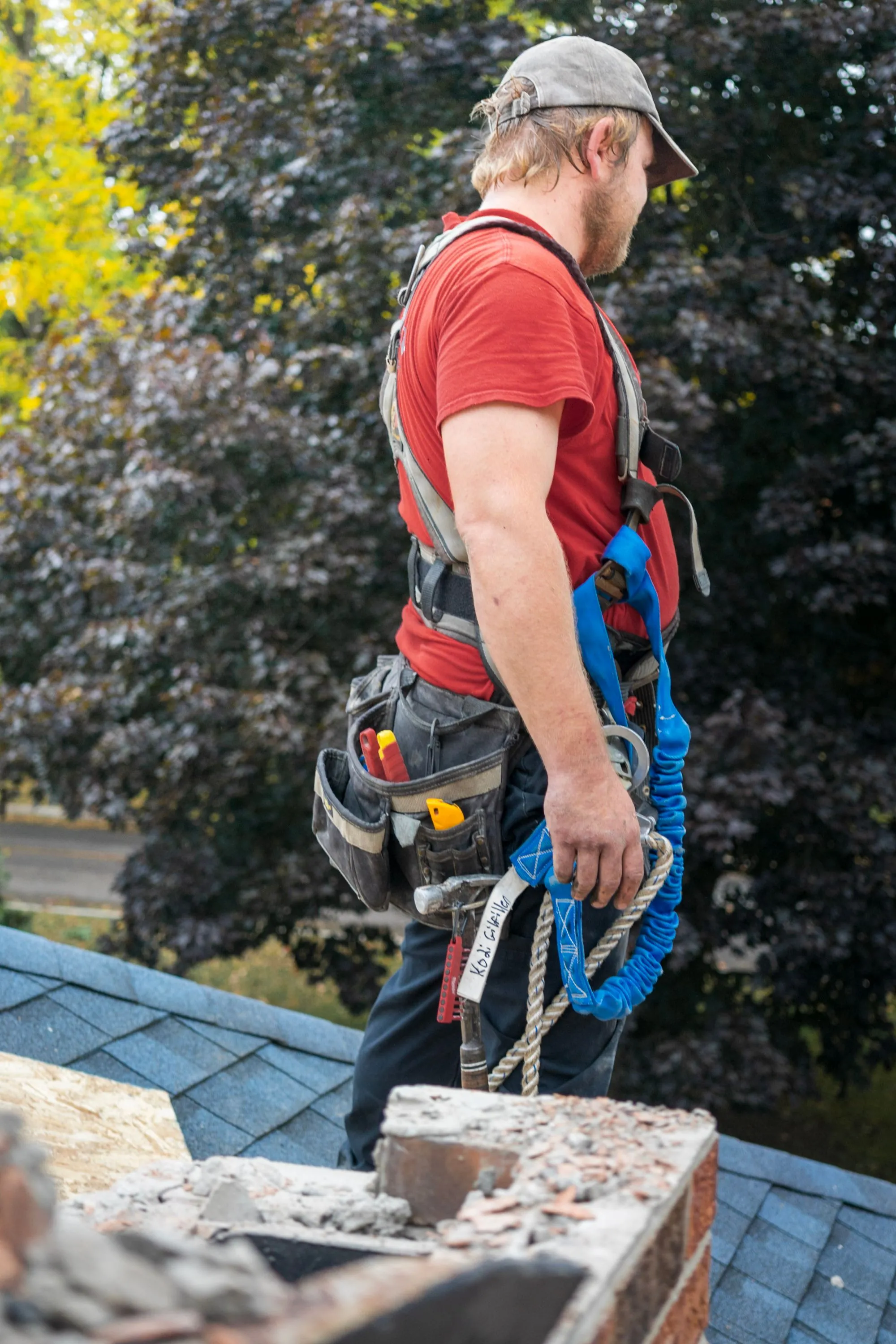 A roofer in a tool belt and harness preparing to work on a residential roof